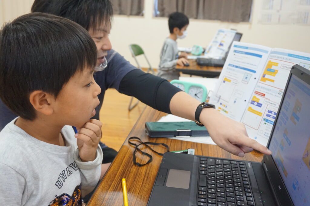 パソコンでプログラミングを教わる子ども