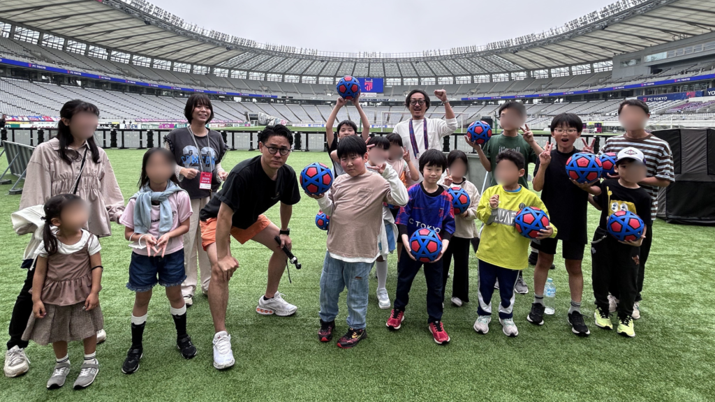 NIJINアカデミーの校外活動でスタジアムの芝生に集まった子どもたちとスタッフ