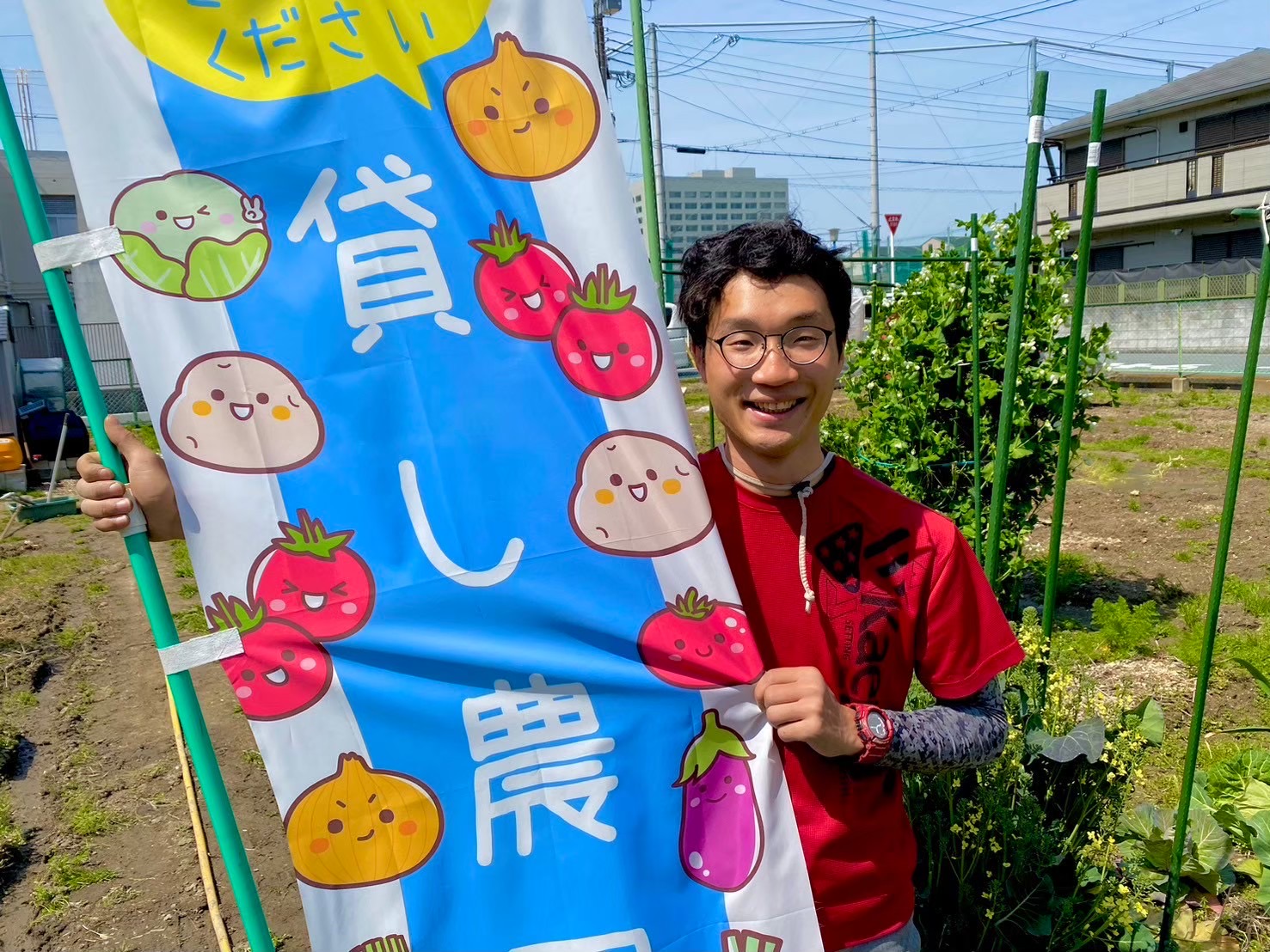「貸し農園」ののぼりのそばで収穫した野菜を持つ人