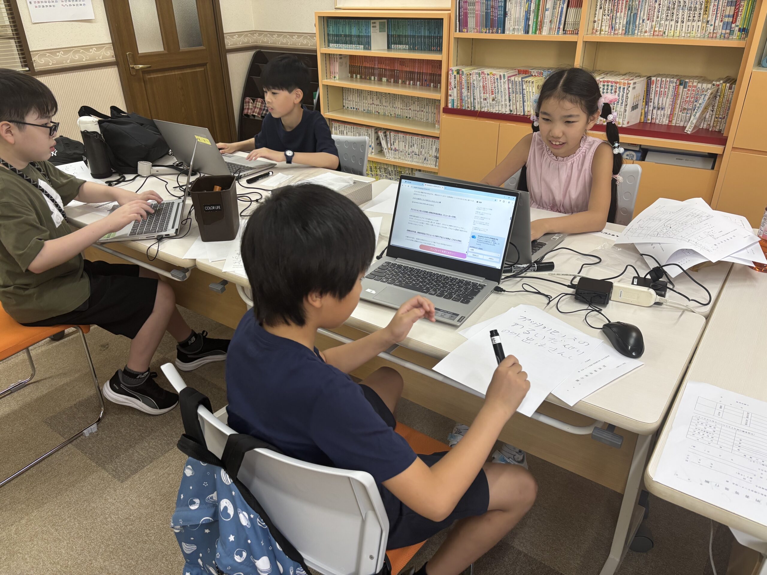 本棚のある部屋でパソコンに向かう子どもたち