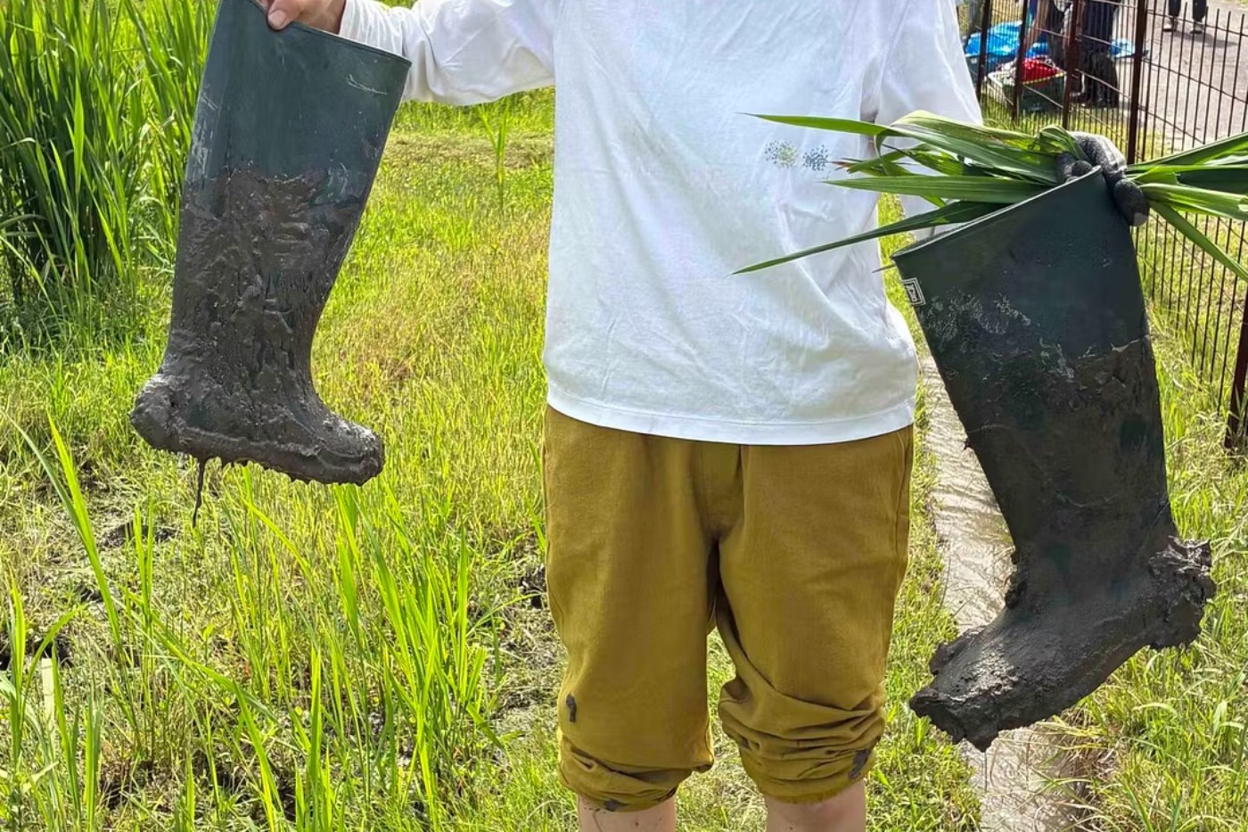 田んぼで泥のついた長靴を持つ子ども