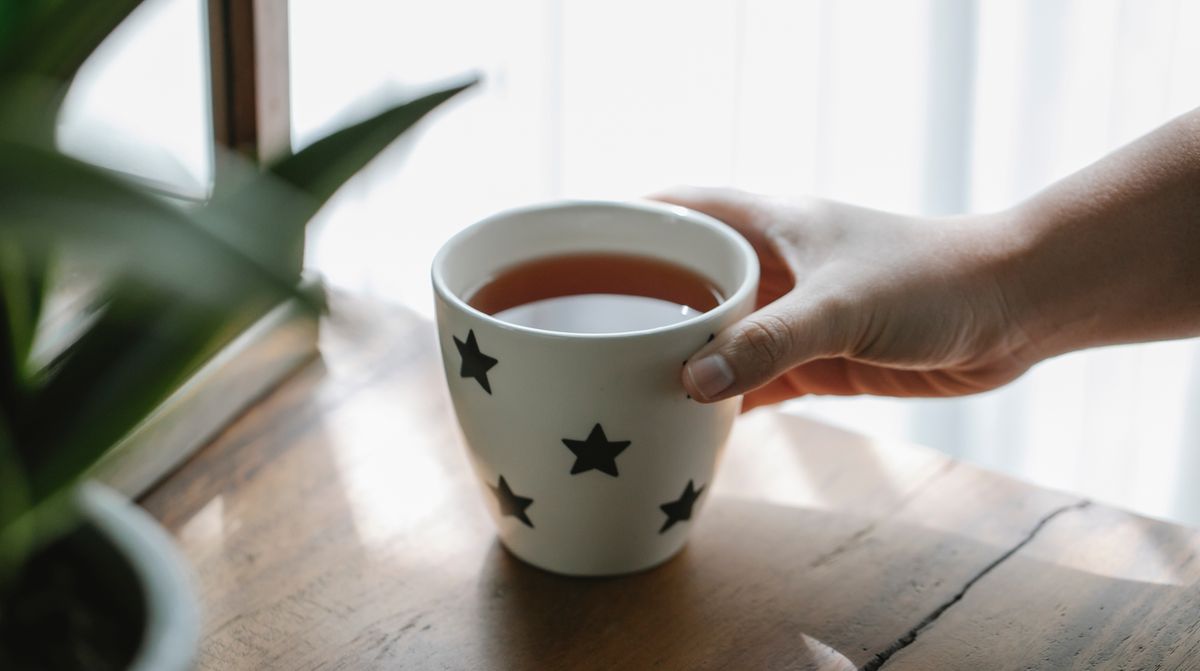 窓辺で紅茶のカップを持つ手