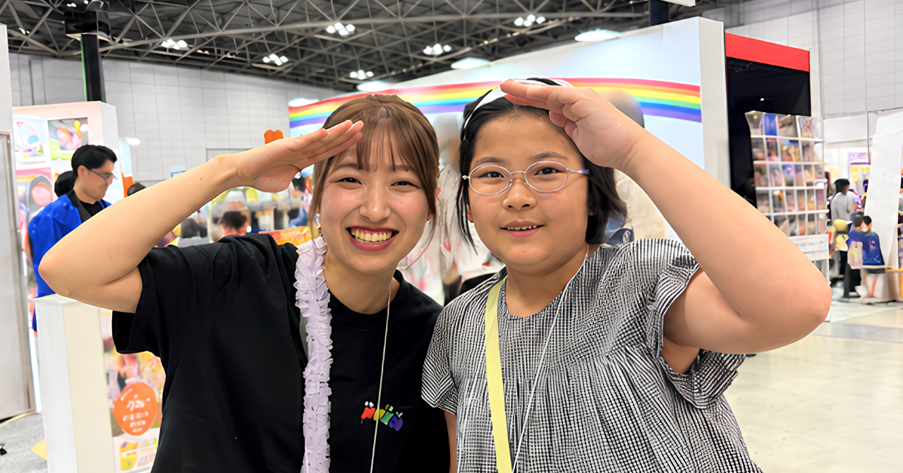 教育の展示会EDIXのNIJINアカデミーブースで、スタッフと子どもが笑顔で一緒にポーズをとっているようす